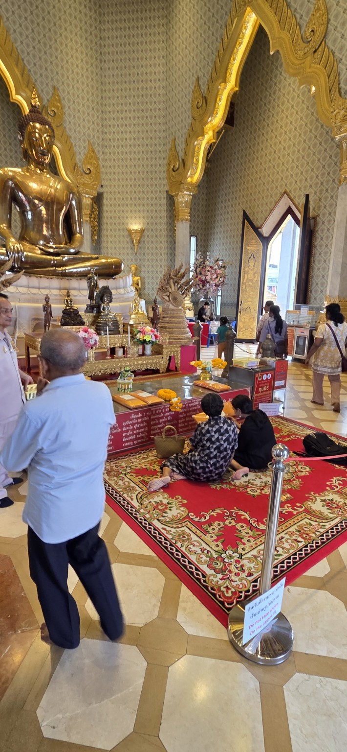 Visitors seated before a golden Buddha inside the temple
